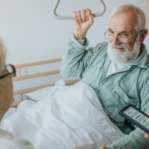 Senior patient gets up from the hospital bed by helping himself with a special handle